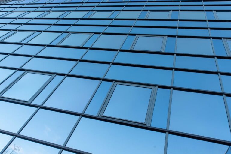 A sleek and reflective blue glass facade of a modern office building demonstrating architecture's clean lines and minimalism.