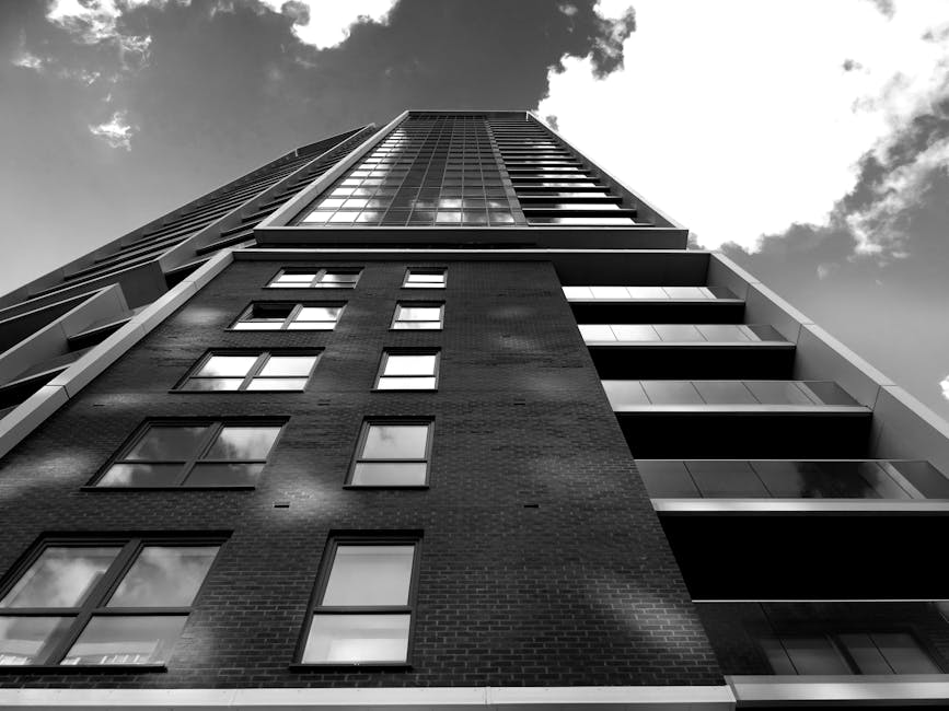 Black and white view of a modern skyscraper with reflective glass and steel architecture against a cloudy sky.